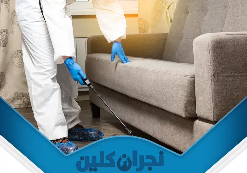 رش مبيدات بنجران 0566353695 نجران كلين عامل شركتنا يرتدي زيًا واقيًا يرش كنبة باستخدام جهاز رش، مما يشير إلى خدمة مكافحة حشرات بنجران أو تنظيف عميق للمفروشات من قبل شركة نجران كلين.