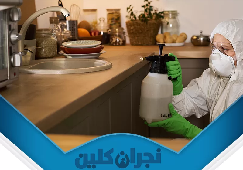 رش مبيد حشرات بنجران 0566353695 نجران كلين تُظهر الصورة فنيًا بزي واقٍ يستخدم بخاخ ضغط يدوي لمكافحة حشرات في المطبخ، ما يعكس خدمات نجران كلين الآمنة والفعّالة في القضاء على الآفات