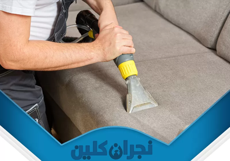 تنظيف الكنب من البقع بنجران 0566353695 نجران كلين تُظهر الصورة عملية احترافية لـ تنظيف الكنب من البقع بنجران، حيث يقوم عامل متخصص باستخدام جهاز تنظيف حديث لإزالة الأوساخ والبقع بفعالية من قماش الكنب، مما يضمن استعادة نظافته وجماله.